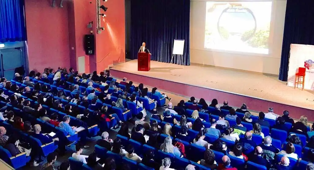 Alessandro Ferrari sul palco durante un corso di formazione sulla comunicazione efficace e tecniche di vendita a Sirmione, davanti a un ampio pubblico di imprenditori e manager.